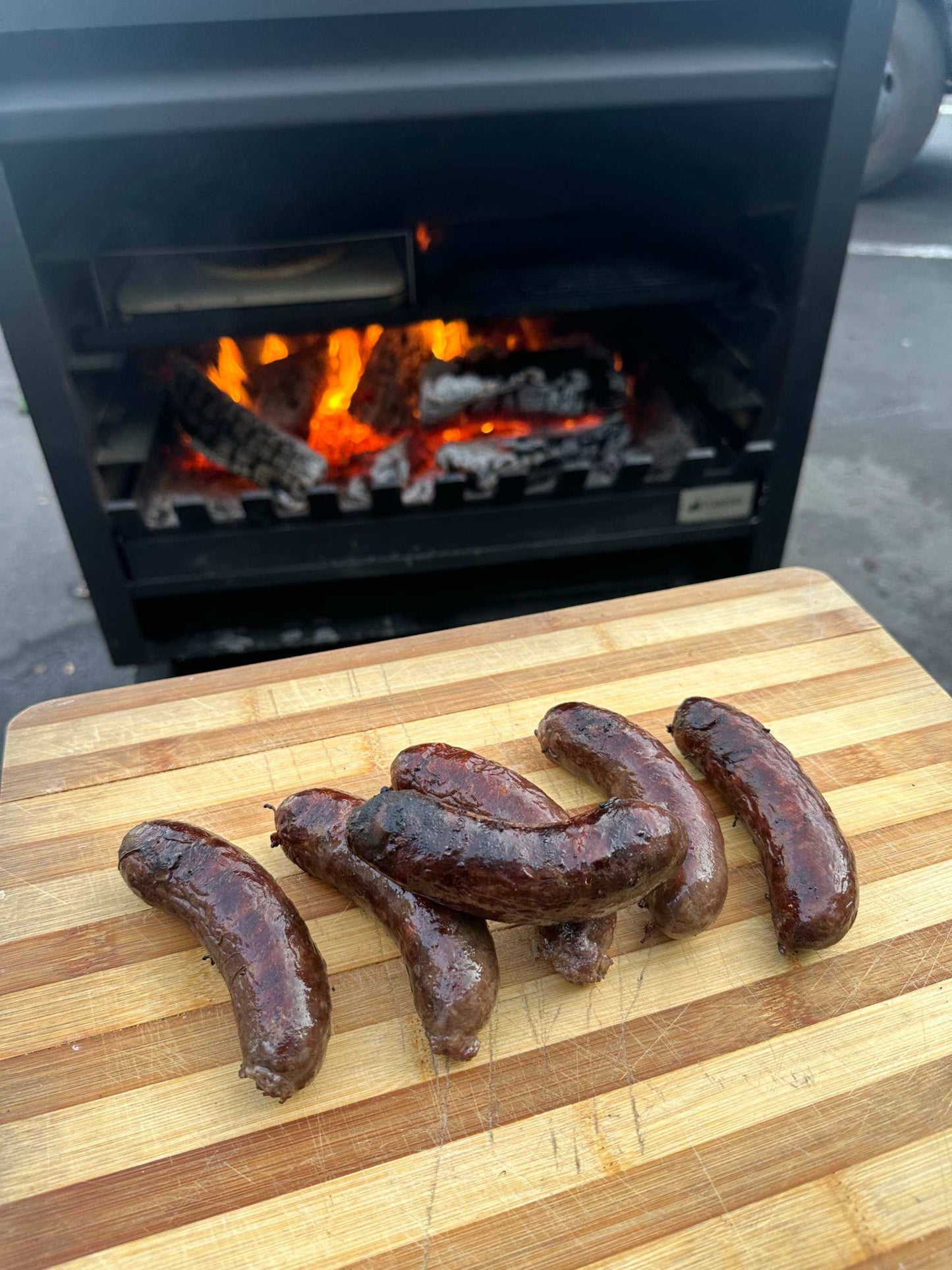 Outdoor Onflame 900 fireplace with grilled sausages on a wooden board.