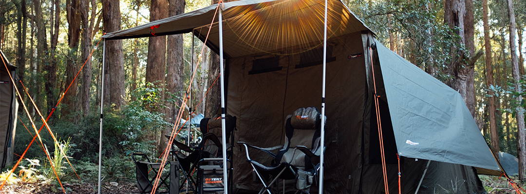 Oztent RV5 tent set up in a forest with chairs under awning.