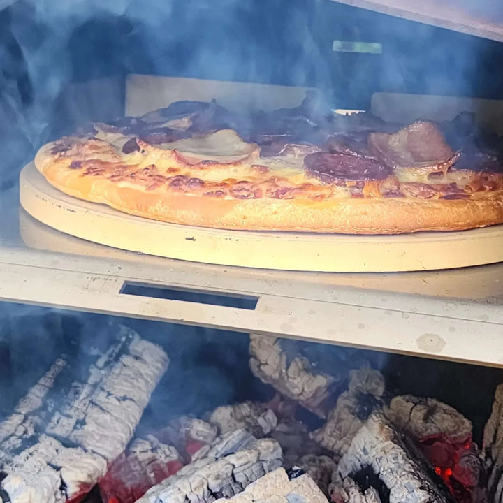Wood-fired pizza cooking on Obelisk outdoor fire with pizza kit including stone and peel.
