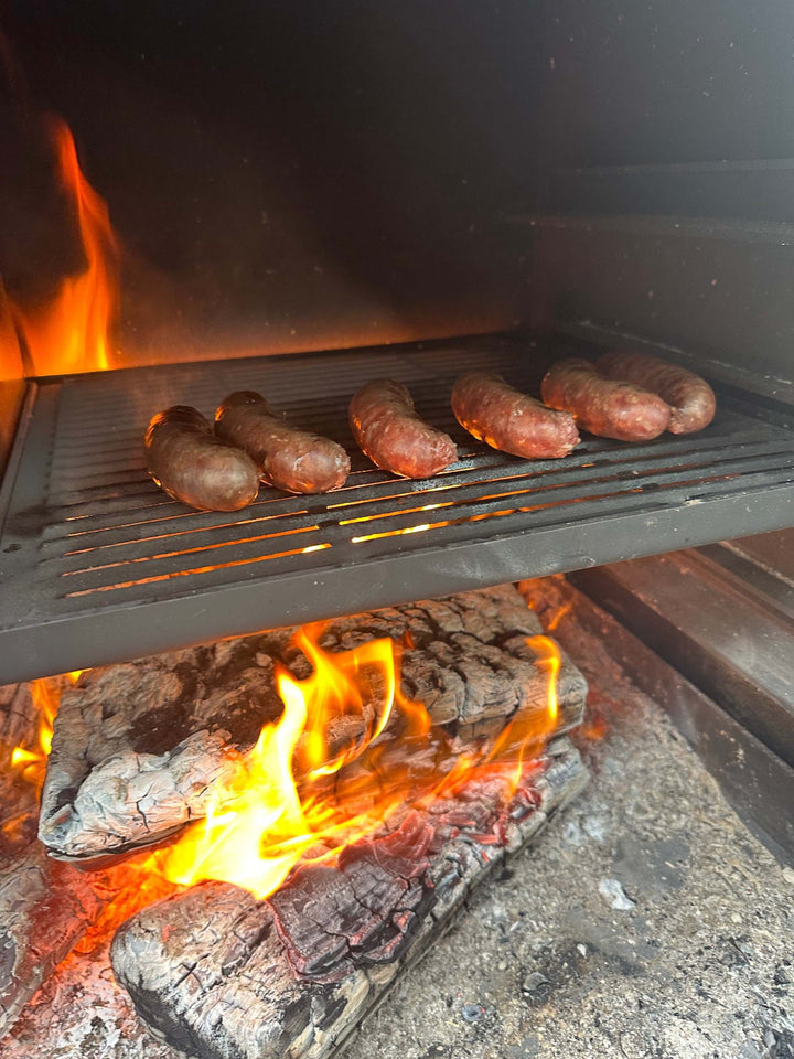 Onflame 900 fireplace grilling sausages over wood fire logs.