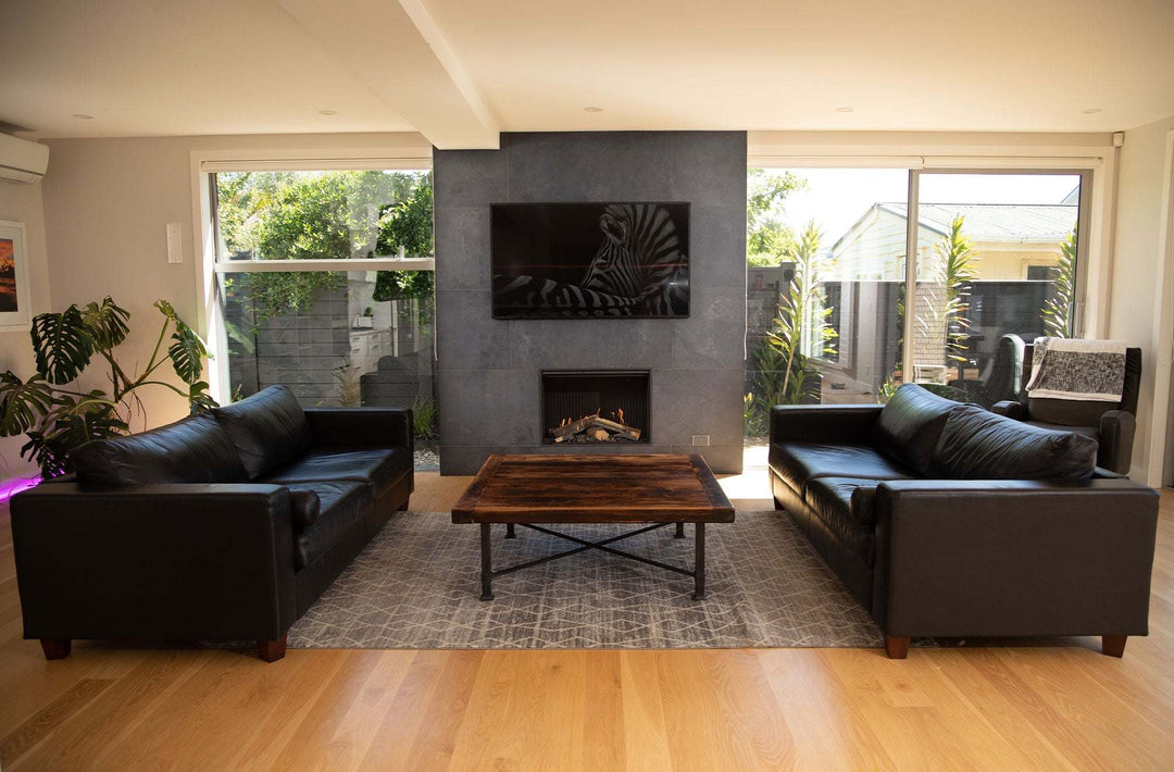 Modern living room with Rinnai Linear 800 gas fireplace installed on a sleek wall, surrounded by black leather sofas and a wooden coffee table.
